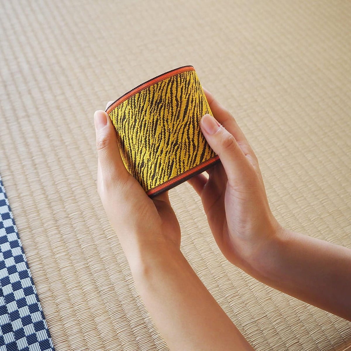 A person's hands holding a yellow and black striped object, which appears to be a wallet or a small bag.