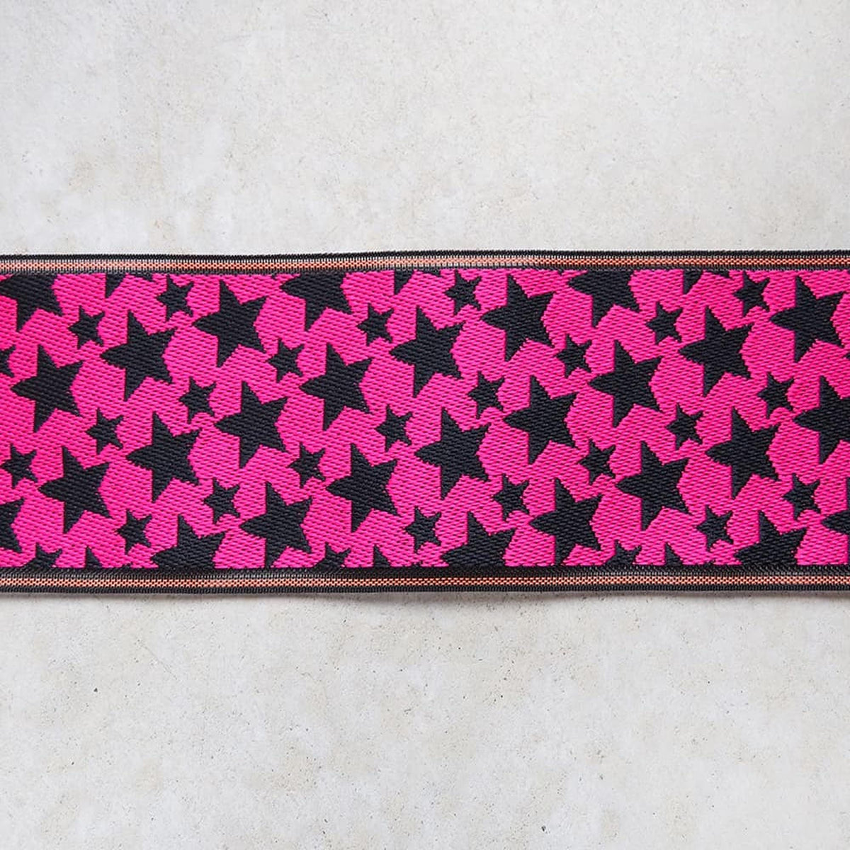 A close-up view of a ribbon with a repeating pattern of pink stars on a black background.