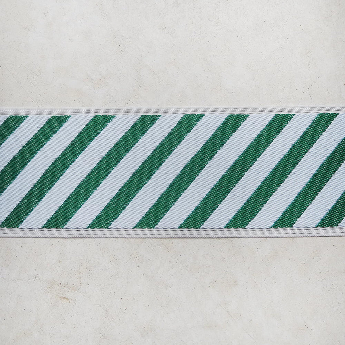 A close-up view of a white and green striped fabric or ribbon, with the fabric arranged in a diagonal pattern.