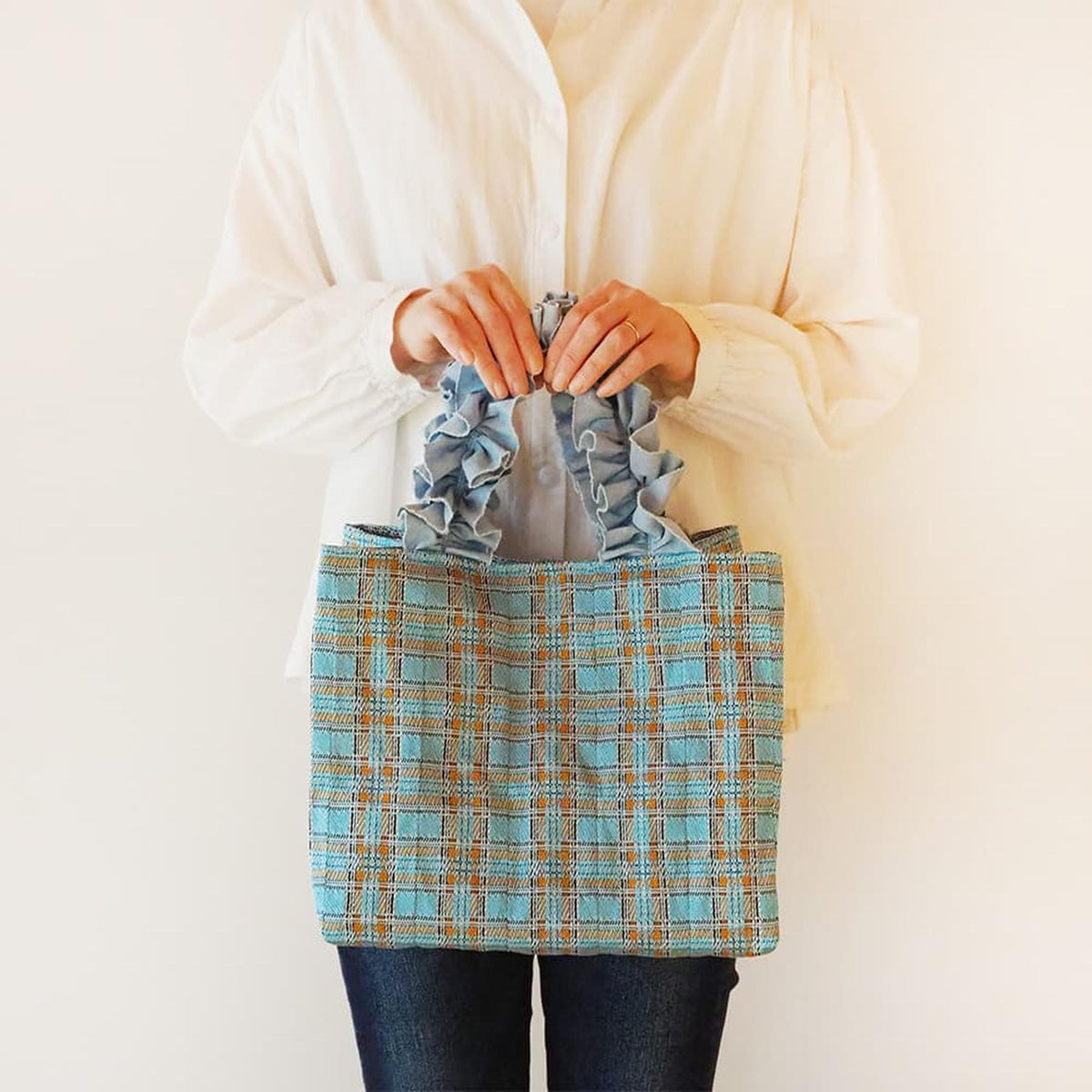 A person is holding a blue and orange checkered handbag in front of them.