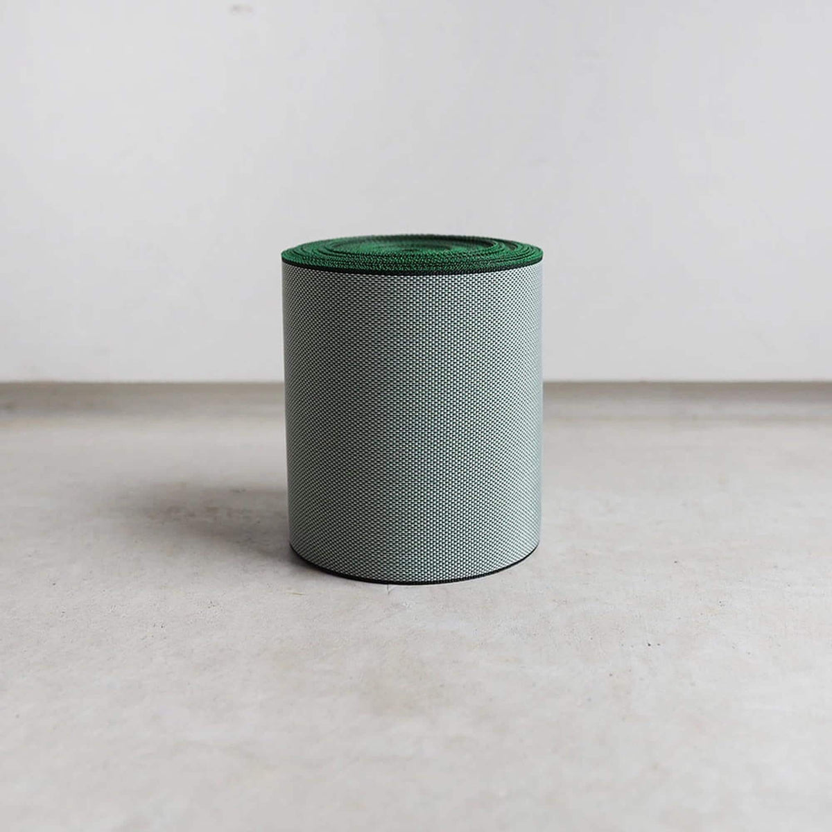 A cylindrical object with a green top, standing alone on a gray surface against a white background.