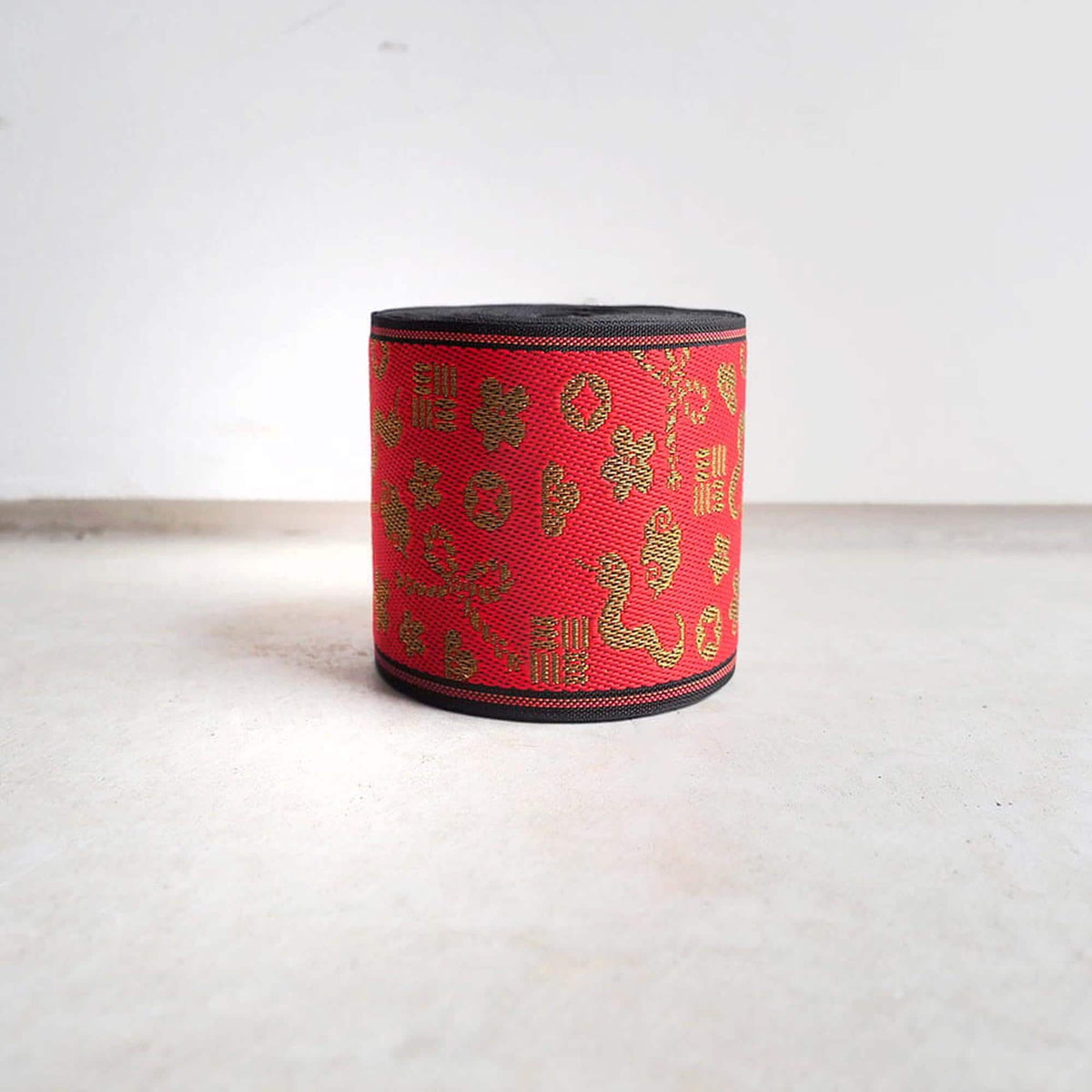 A red and gold patterned object, possibly a container or decorative item, is sitting on a white surface against a plain white background.