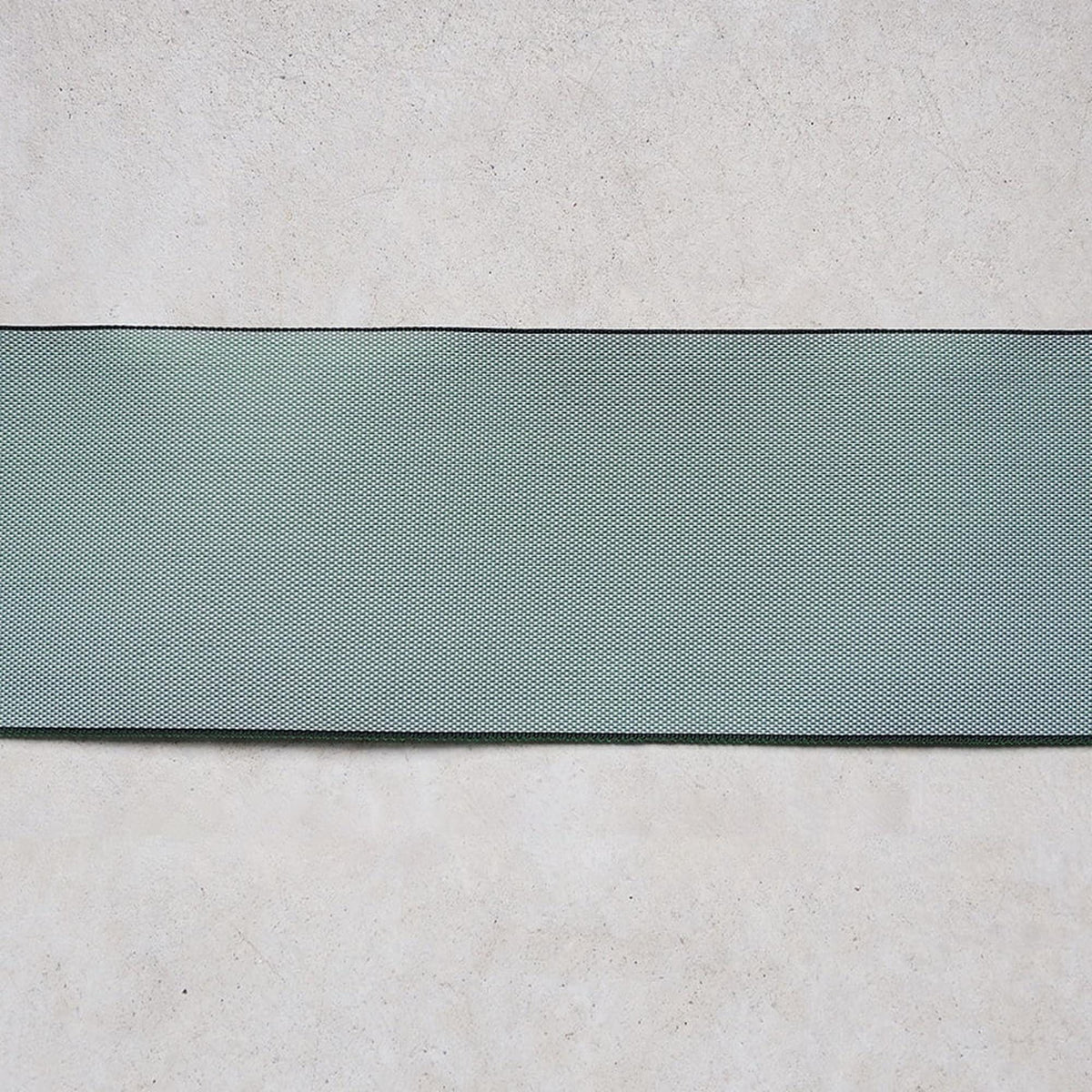 a green fabric or material with a diagonal pattern, placed on a plain, light-colored surface.