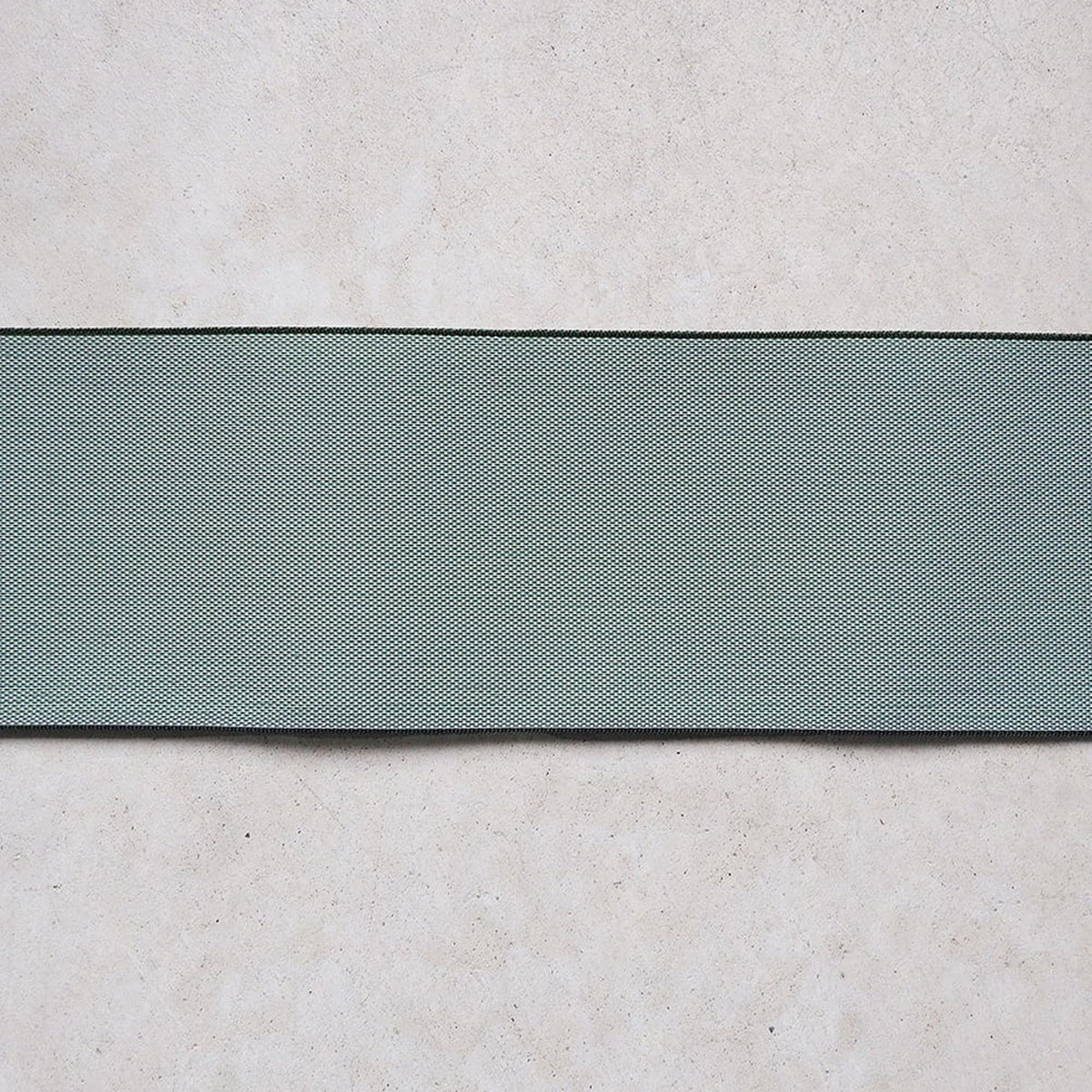 a close-up view of a green fabric or material with a textured pattern, placed on a plain, light-colored surface.