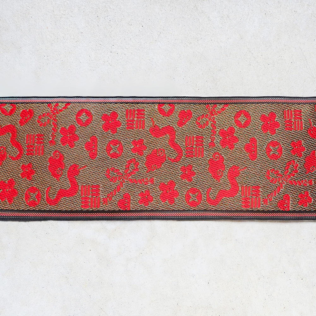 a decorative fabric with a repeating pattern of red and brown shapes, including flowers, leaves, and geometric designs.