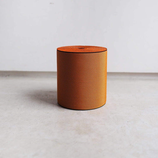 A cylindrical orange object with a textured surface is standing alone on a plain white surface.