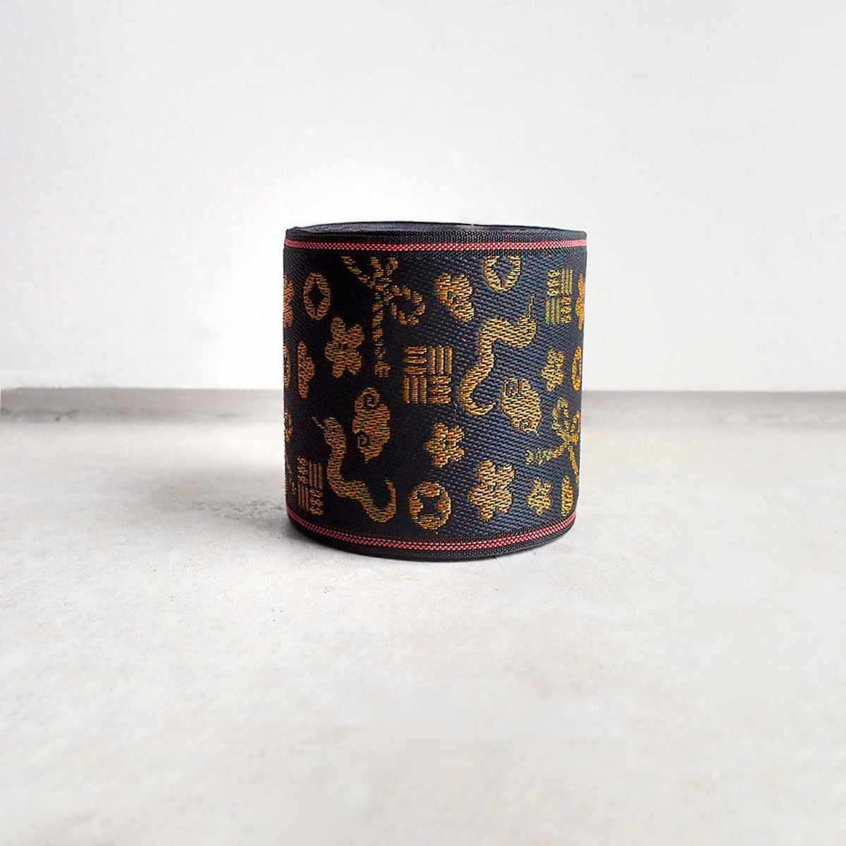 A black and gold decorative object with a pattern of gold and black shapes, such as flowers, leaves, and geometric designs, is displayed on a white surface.