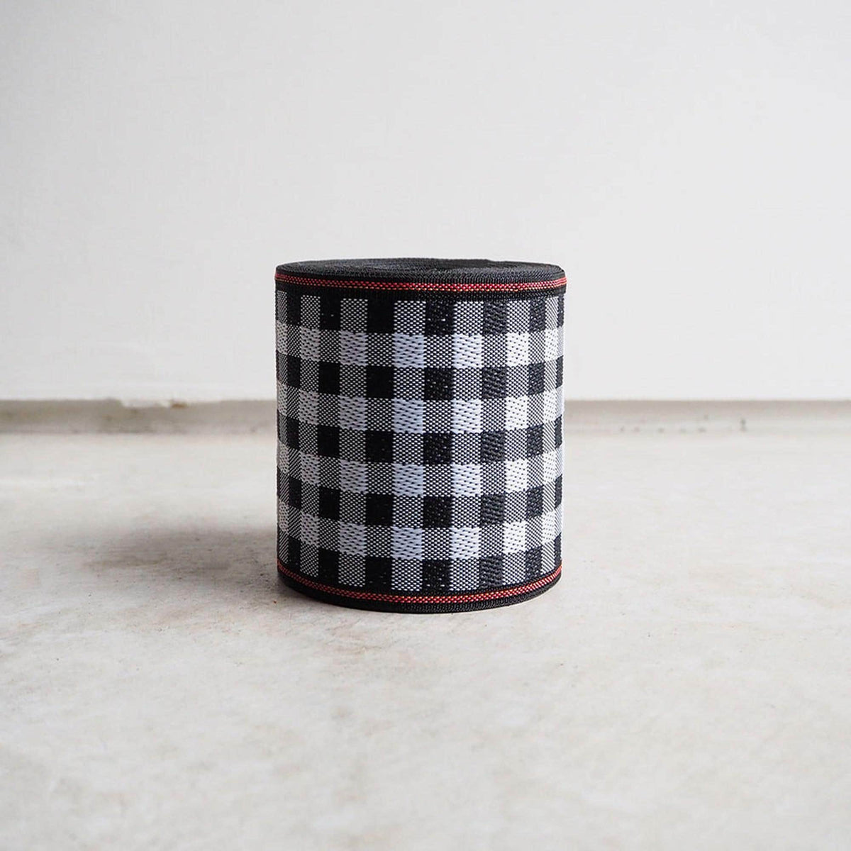 A cylindrical object with a black and white checkered pattern, featuring a red border around the top edge.