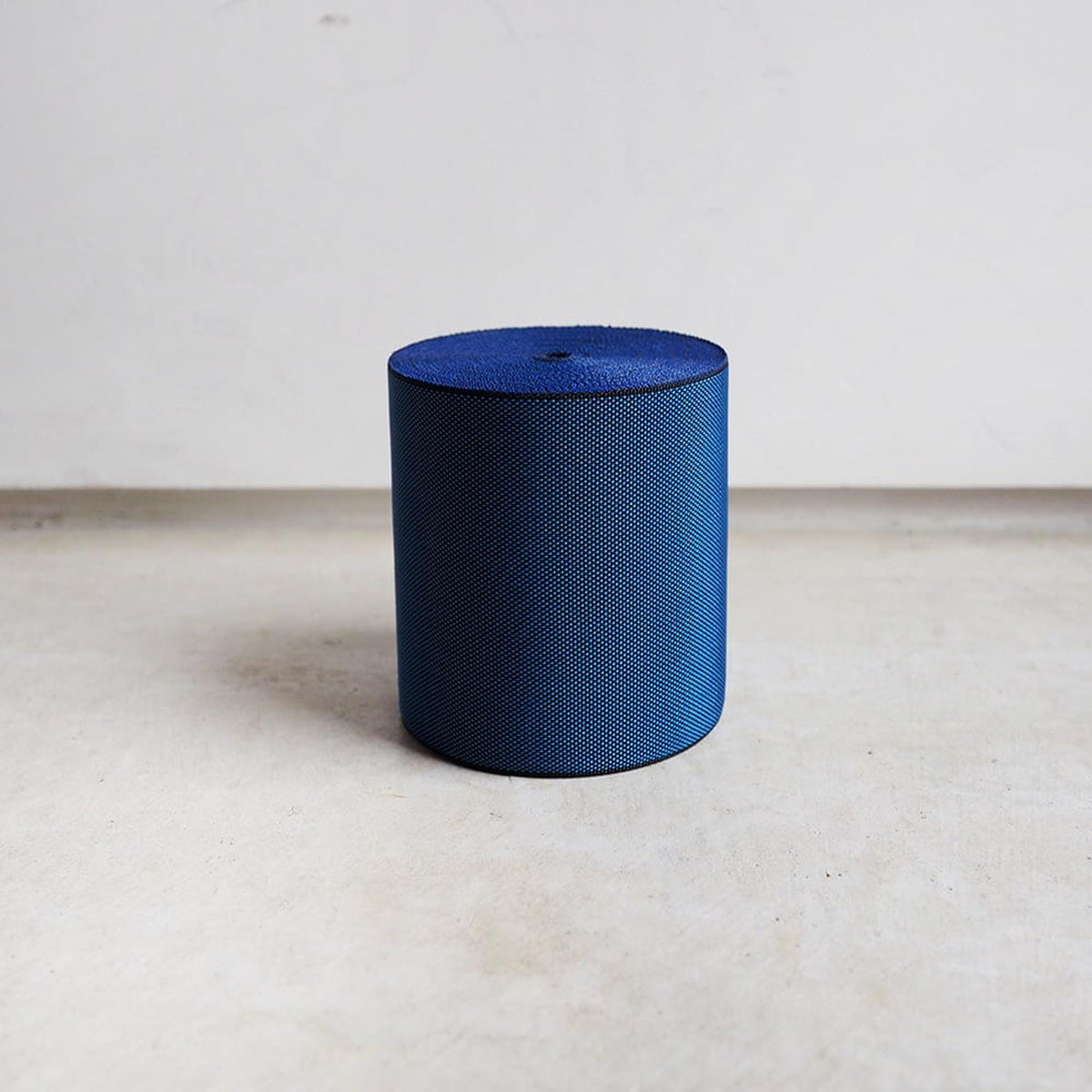 A blue cylindrical object with a textured surface, standing alone on a plain white surface.