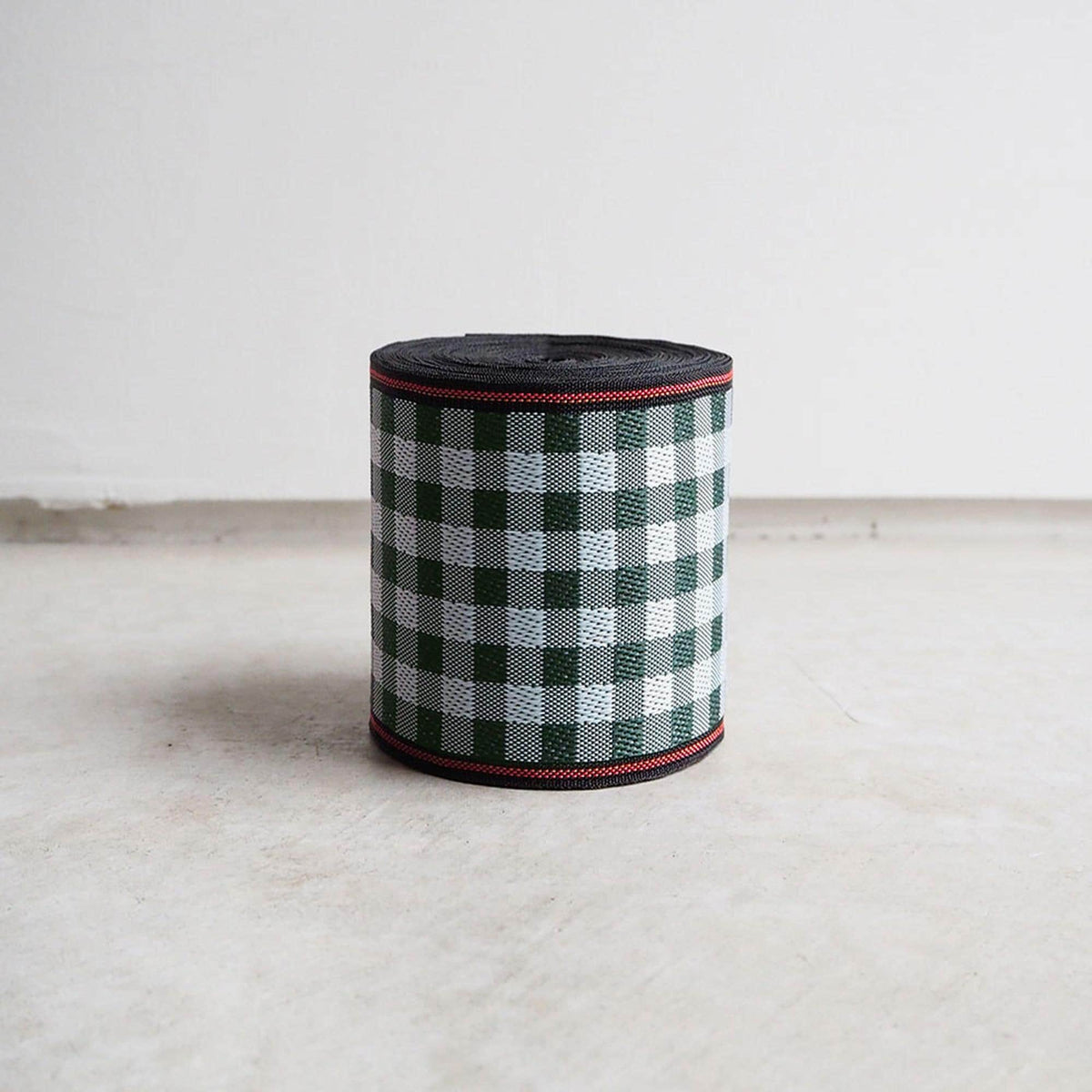 A cylindrical object with a checkered pattern in green and white colors, sitting on a white surface against a plain background.