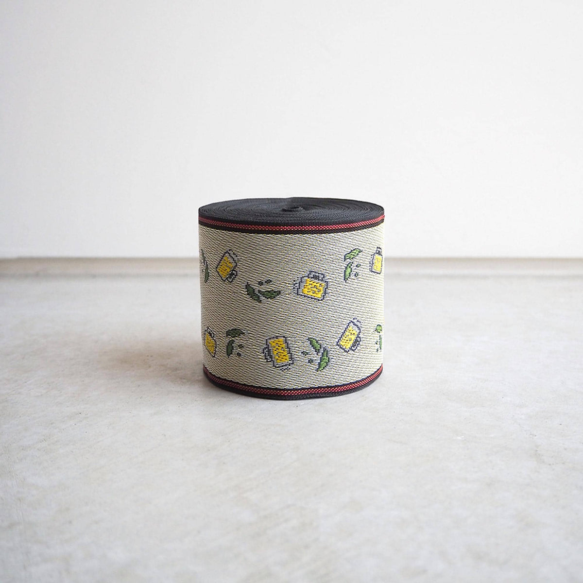 A cylindrical object with a pattern of yellow and green shapes on a beige background, sitting on a white surface.