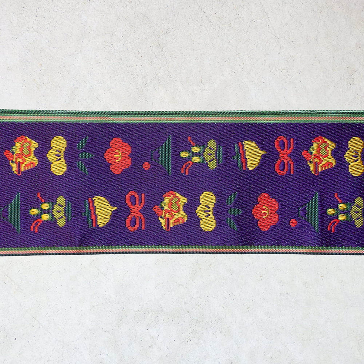 a vibrant purple fabric with a repeating pattern of colorful flowers and leaves in shades of red, yellow, and green.