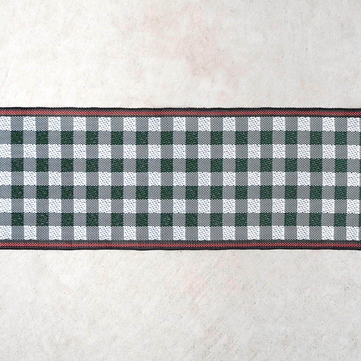 A checkered table runner with a red border is displayed against a plain beige background.
