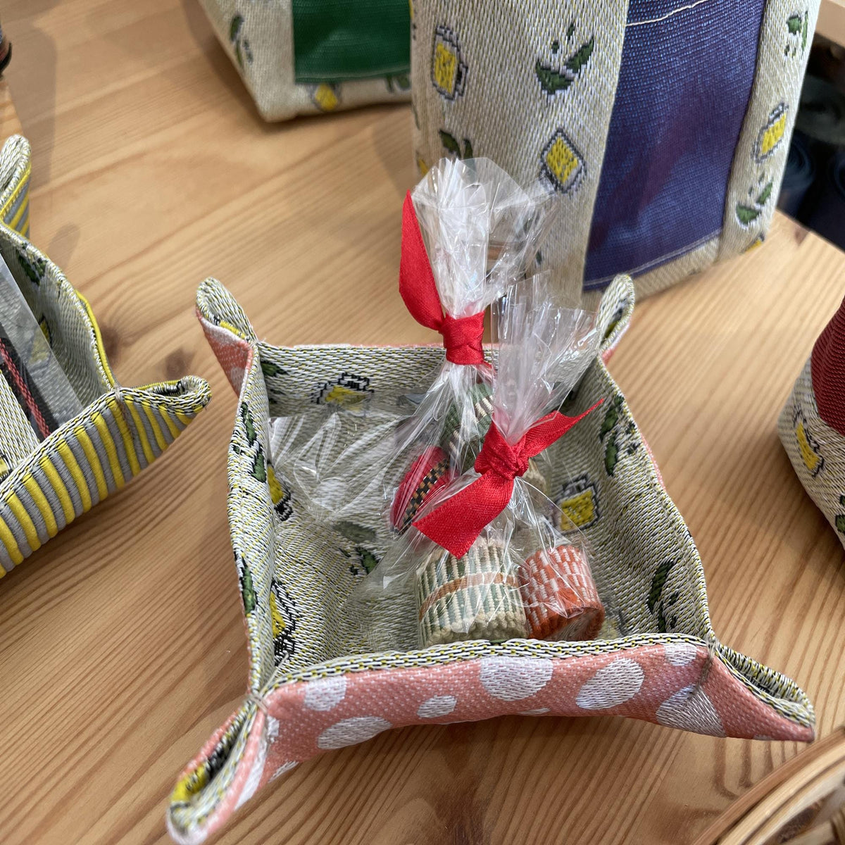 A wooden table with a pink and white patterned tray holding two wrapped items with red ribbons.