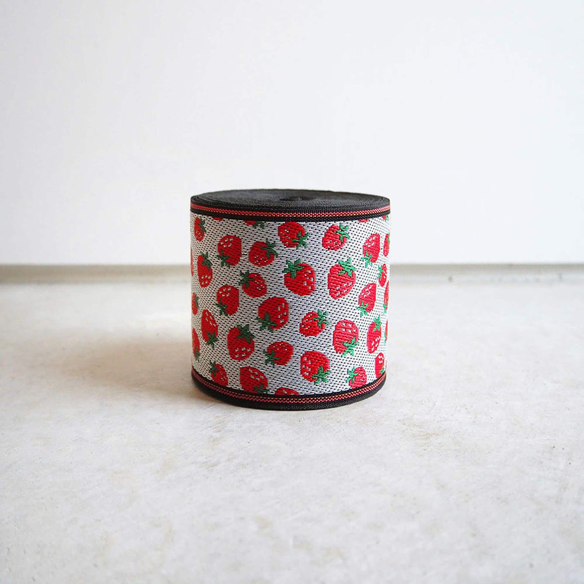 A cylindrical object with a black and red pattern of red strawberries on a white background.