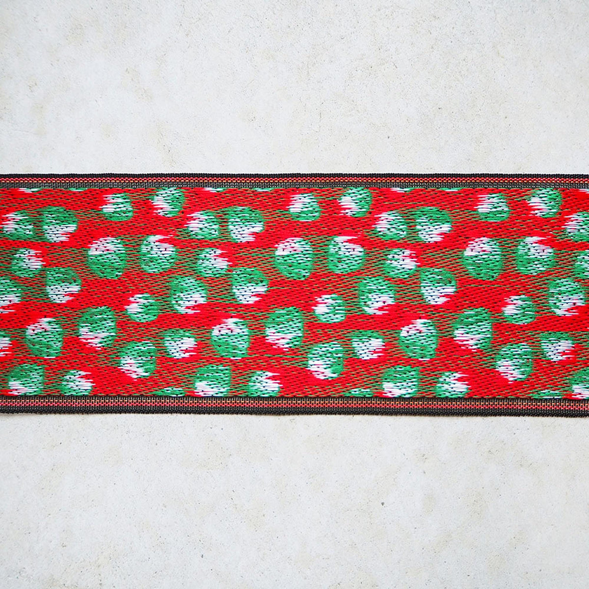 a red and green patterned fabric with a black border, displayed against a white background.