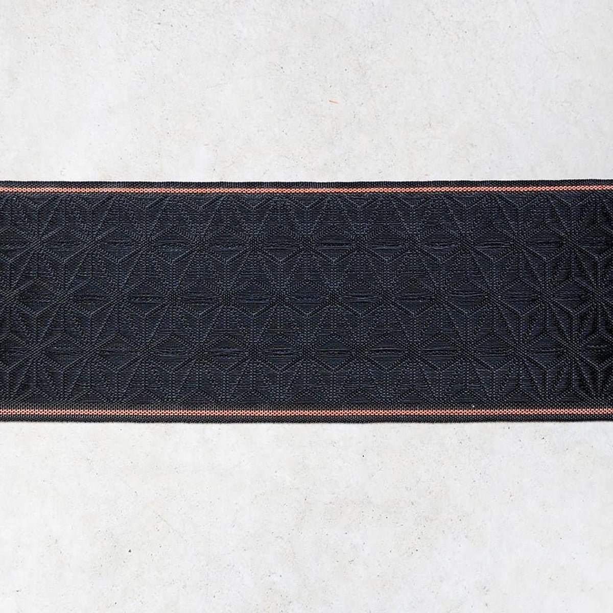 a close-up view of a black fabric with a repeating pattern of geometric shapes, such as diamonds or triangles, arranged in a horizontal line.