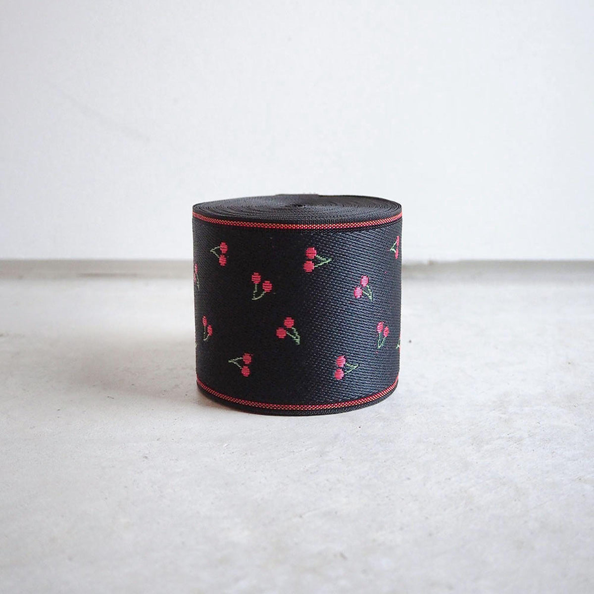 A black ribbon with red cherries printed on it, sitting on a white surface.