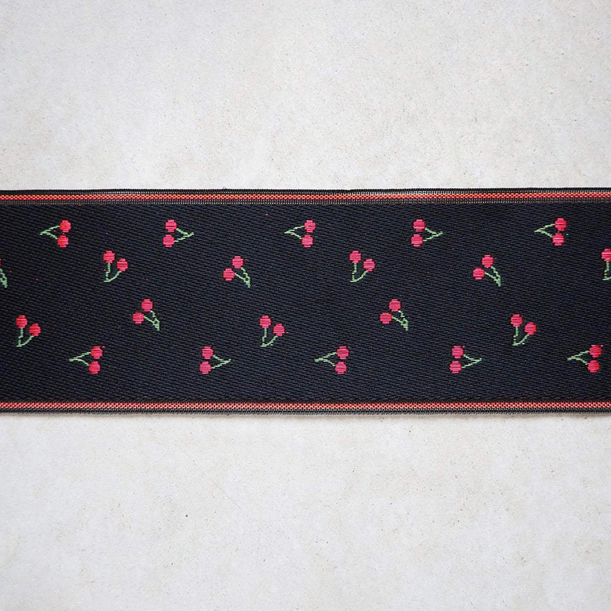 a black fabric with a repeating pattern of red cherries on a white background.