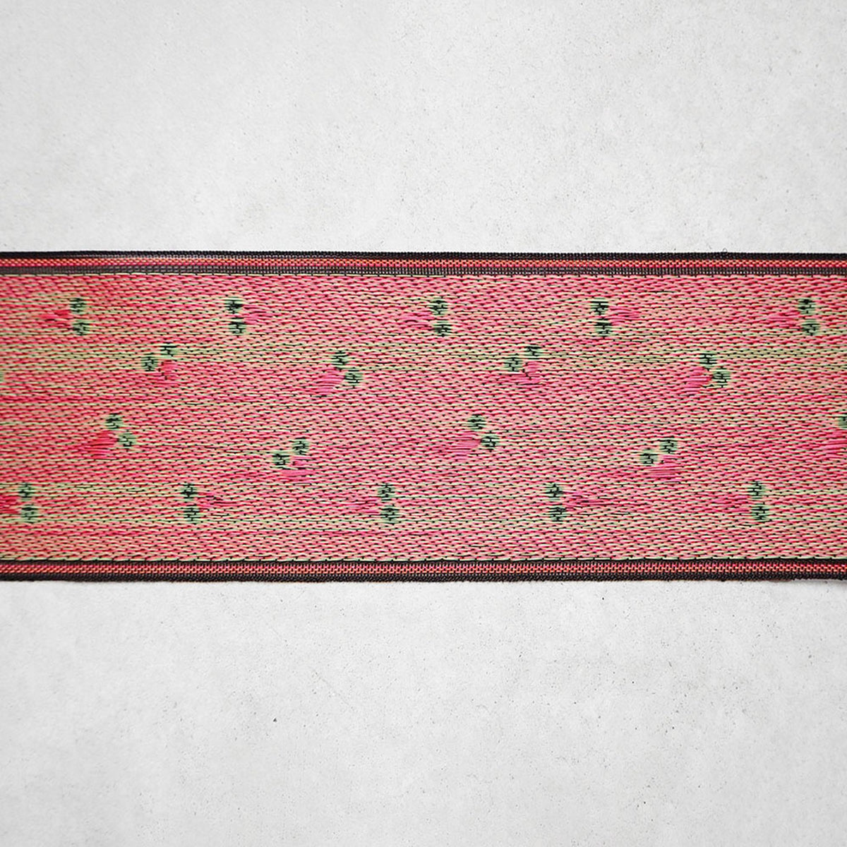 a close-up view of a colorful, textured fabric with a repeating pattern of pink and green flowers or leaves.