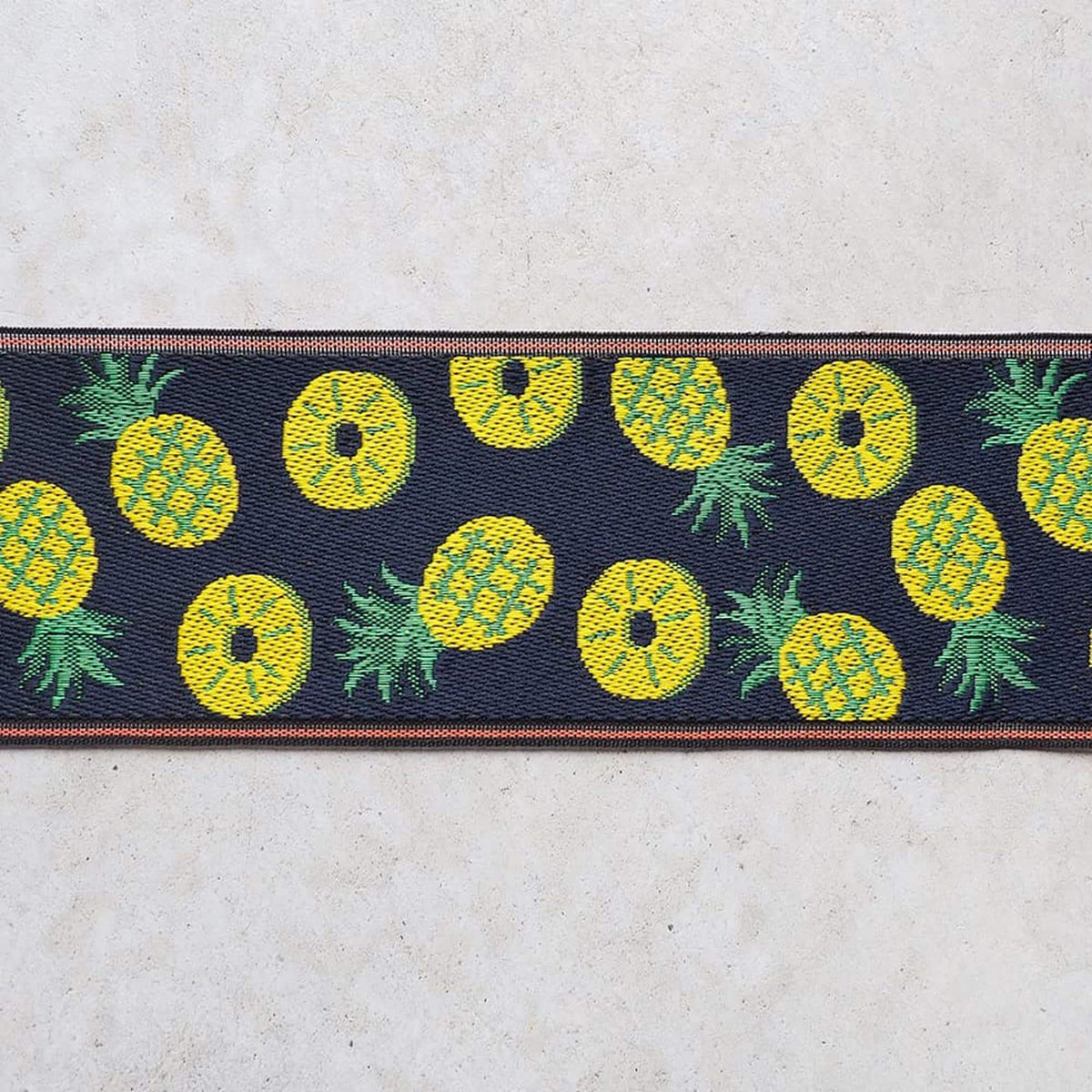 a close-up view of a fabric with a repeating pattern of yellow pineapples on a dark background.