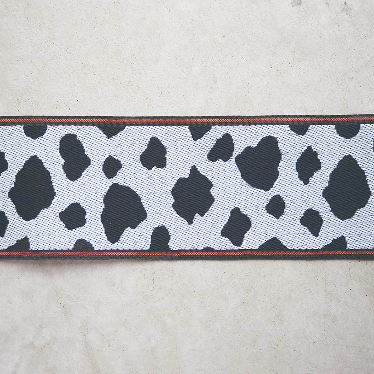 a close-up view of a black and white cow print fabric with a red border.