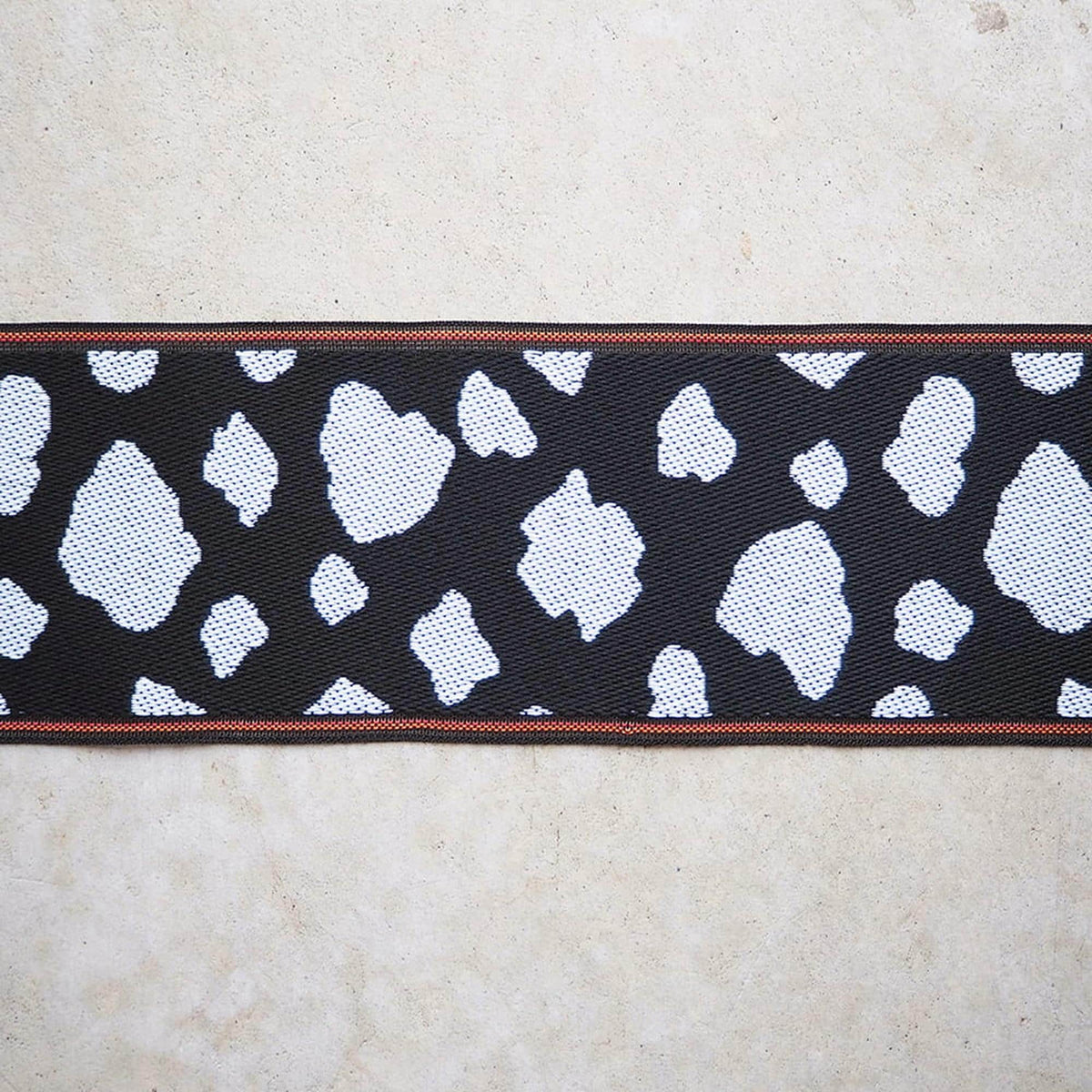 a close-up view of a black and white patterned fabric with a red border, placed on a light-colored surface.