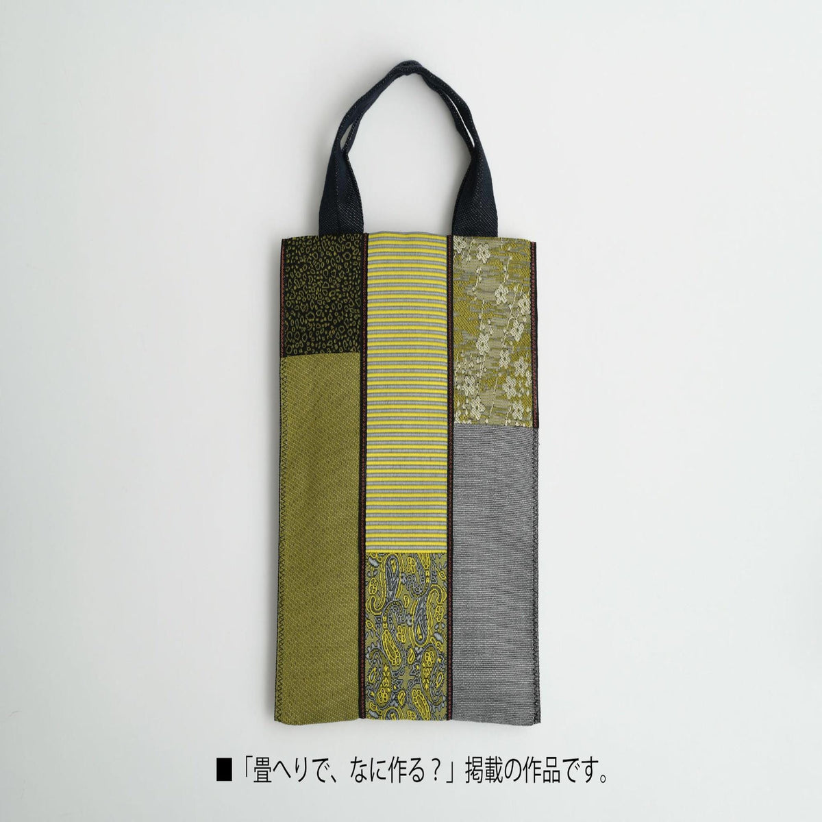 A handbag with a black handle and a black strap, featuring a variety of colorful fabric panels in shades of green, yellow, and gray.