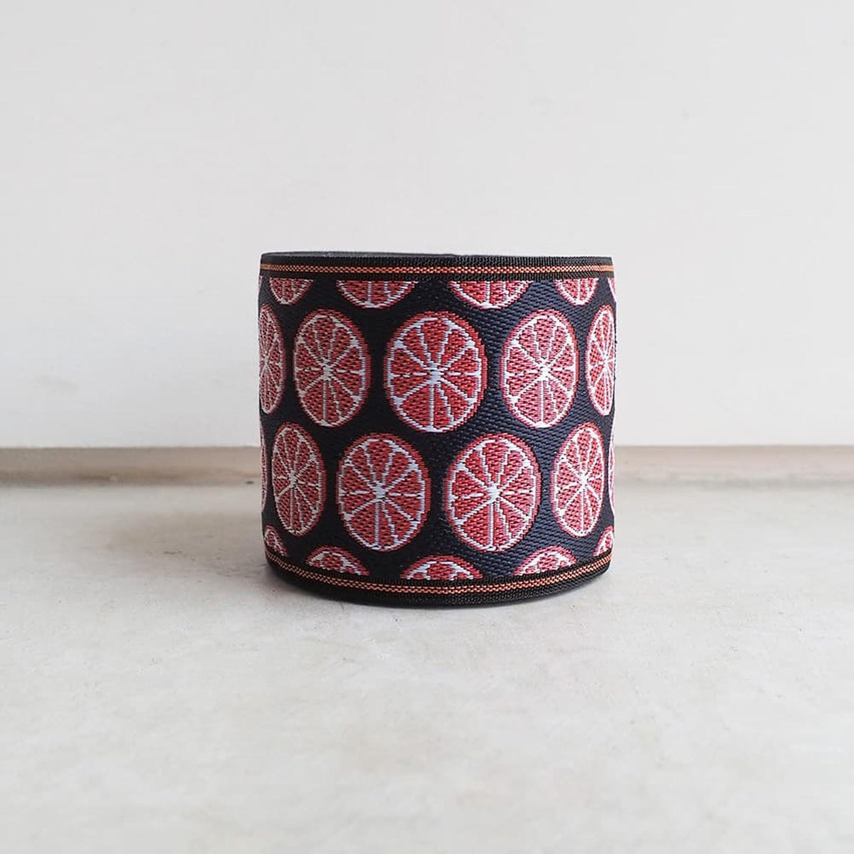 A black and red patterned bracelet or cuff with a repeating design of red and white circles on a black background.