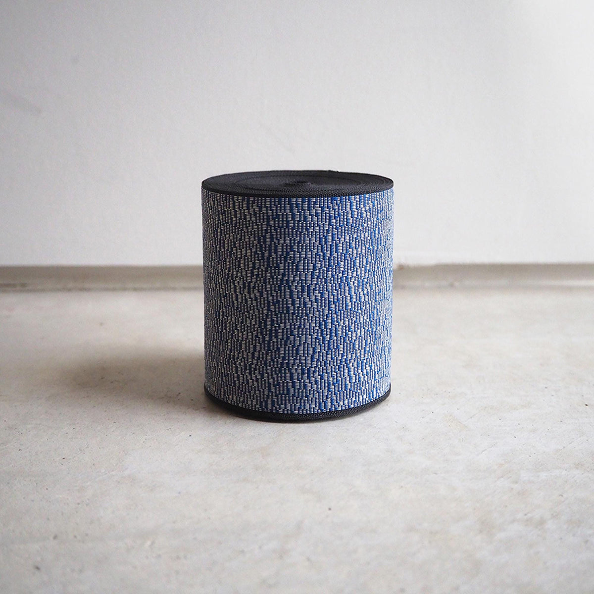 A cylindrical object with a textured blue and white pattern, sitting on a white surface against a plain white background.