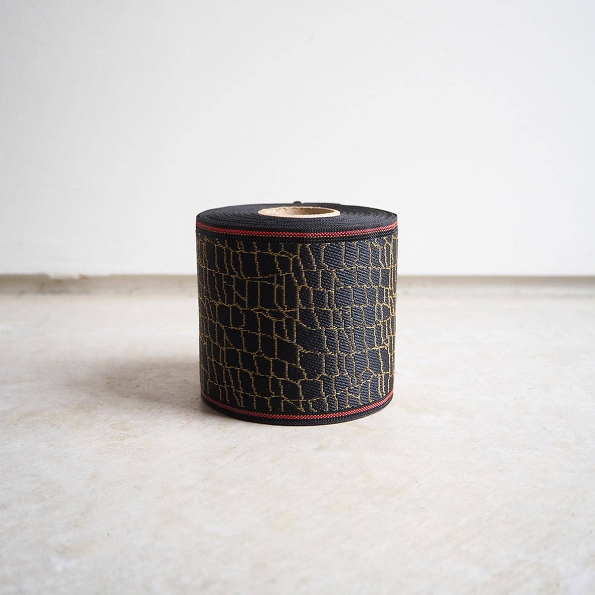 A roll of black and gold patterned tape is sitting on a white surface against a plain white wall.