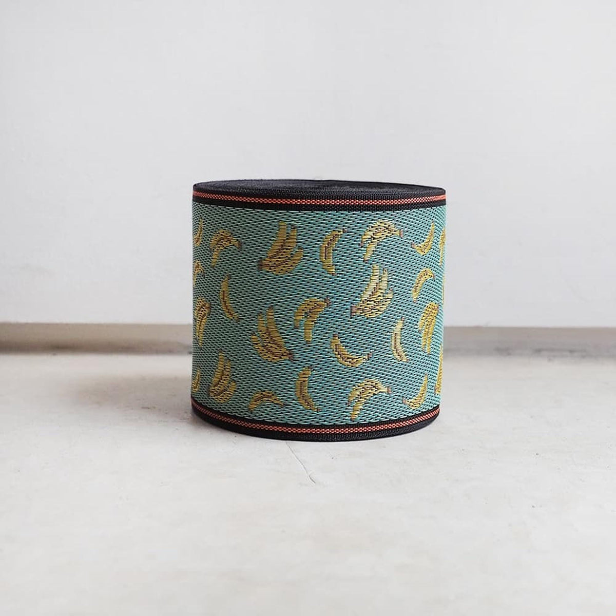 A cylindrical object with a pattern of yellow bananas on a blue background, sitting on a white surface.