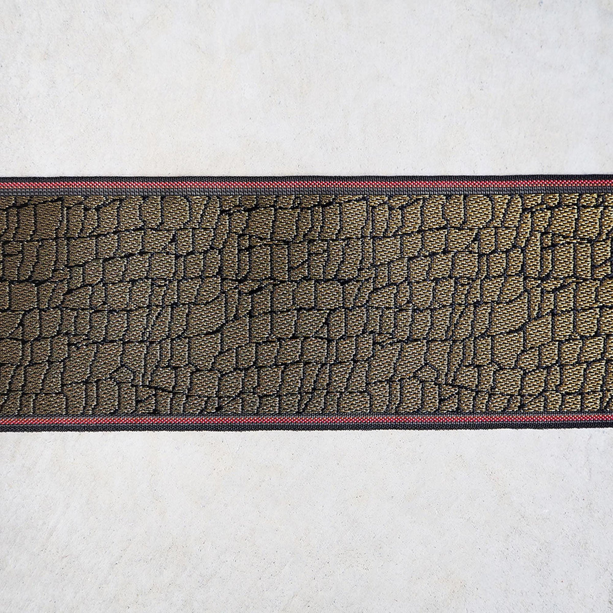 a close-up view of a black and gold patterned fabric with a red border, displayed against a plain white background.