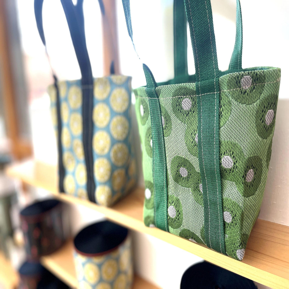two colorful handbags on a shelf, one with a yellow and blue pattern and the other with a green and white pattern.