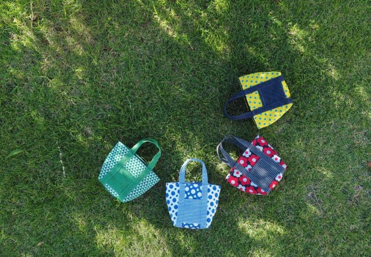 Four colorful handbags in various patterns and colors are arranged on a grassy lawn.