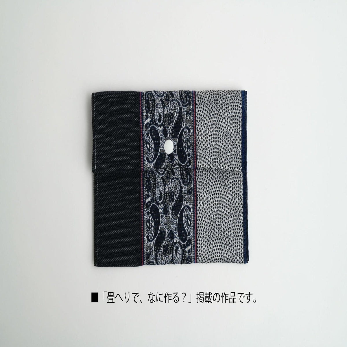 A black and white patterned fabric with a white button in the center, folded in half to create a rectangular shape.