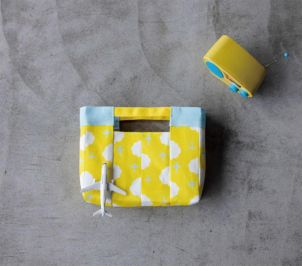 A yellow and blue handbag with a small airplane toy on top, placed on a gray surface.