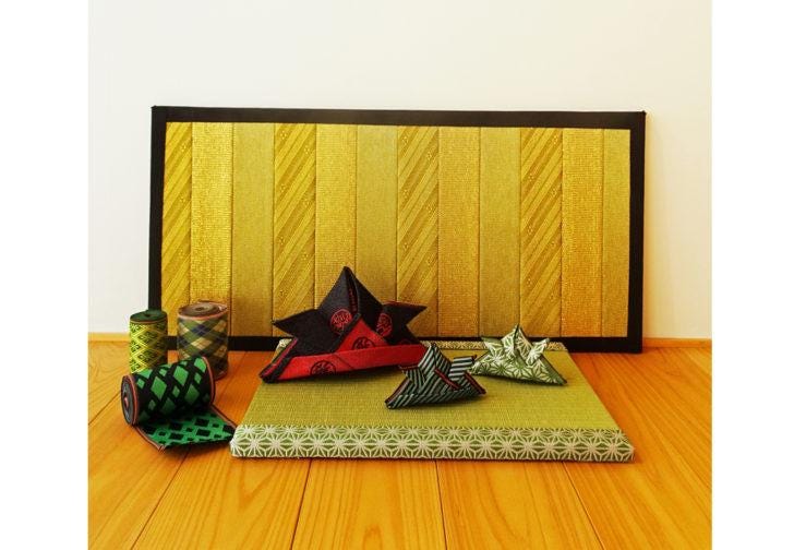 a collection of decorative items, including a large yellow and black striped board, a red and black star-shaped pillow, and several folded origami shapes, all arranged on a wooden floor.