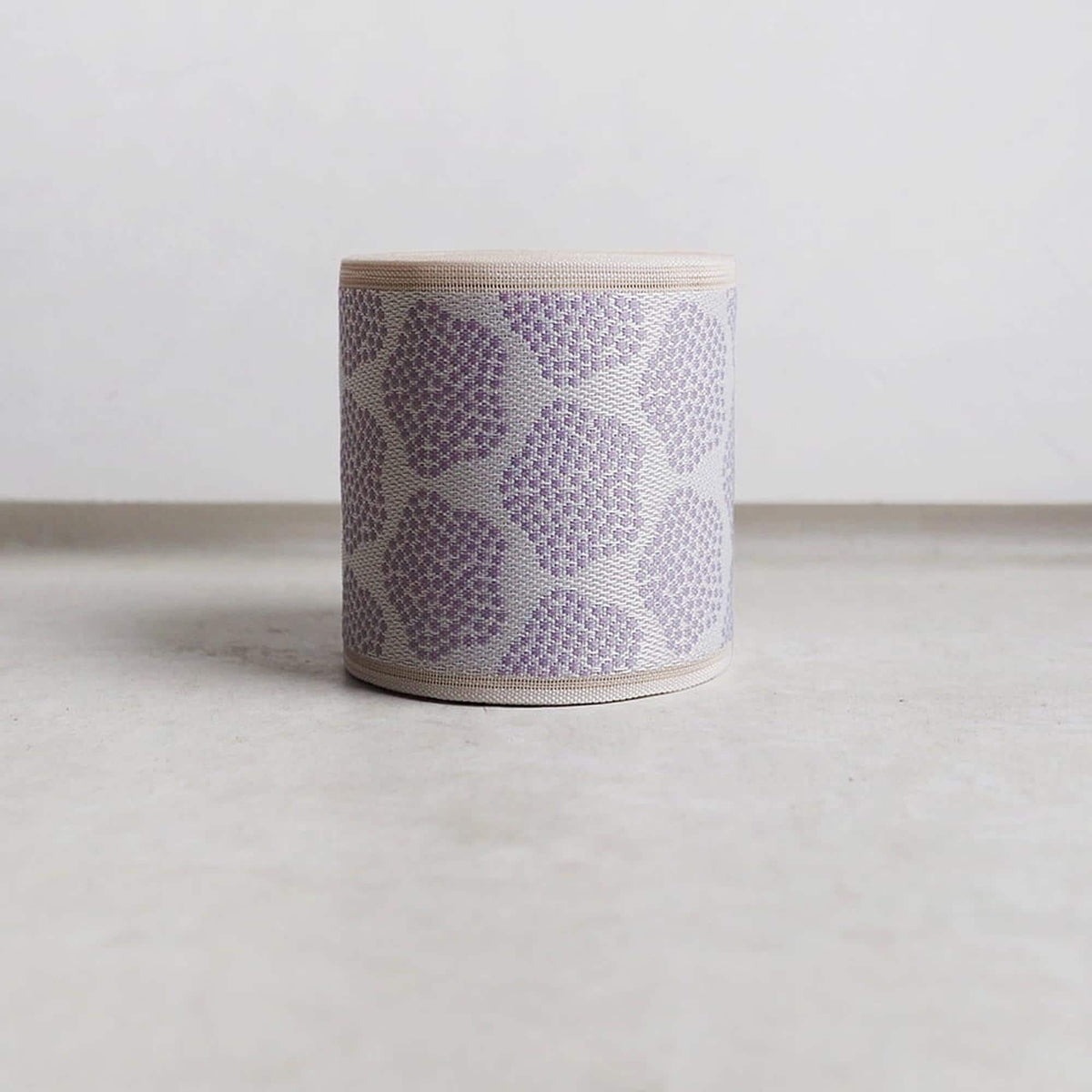 A cylindrical object with a pattern of small circles or dots in shades of purple and white, sitting on a plain surface.