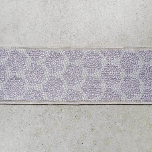 a close-up view of a fabric with a repeating pattern of purple flowers or leaves. The fabric appears to be a type of textile, possibly a piece of clothing or a decorative item. The pattern is intricate and detailed, with the flowers or leaves arranged in a repeating design across the fabric.