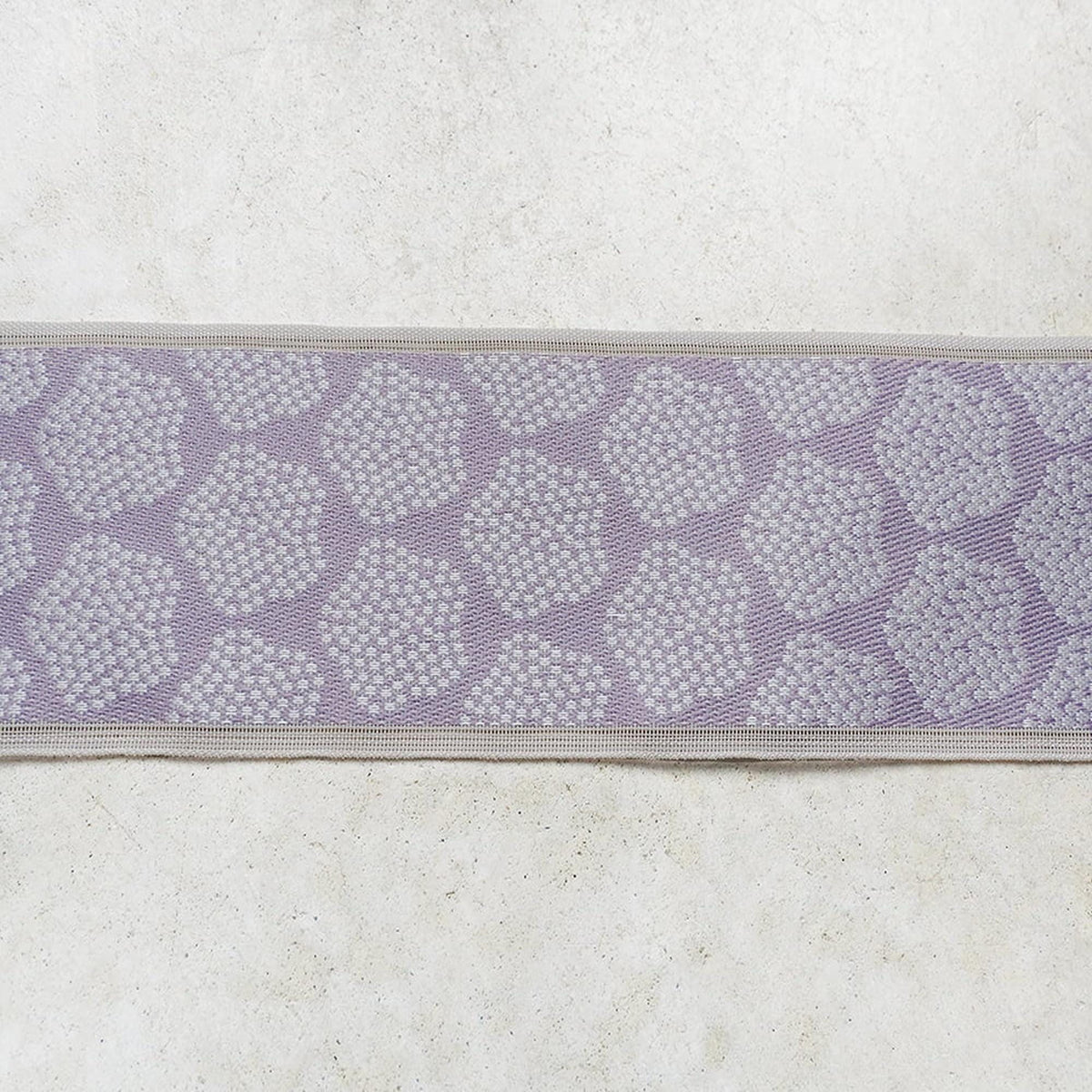 a close-up view of a decorative fabric with a repeating pattern of small white circles or dots on a light purple background.