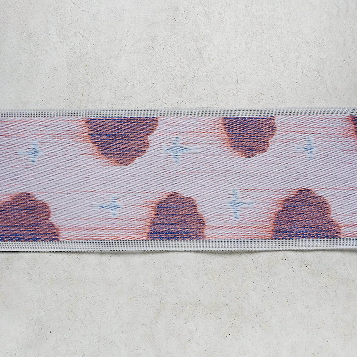 a close-up view of a fabric with a repeating pattern of red and blue shapes, resembling a cloud or a design.