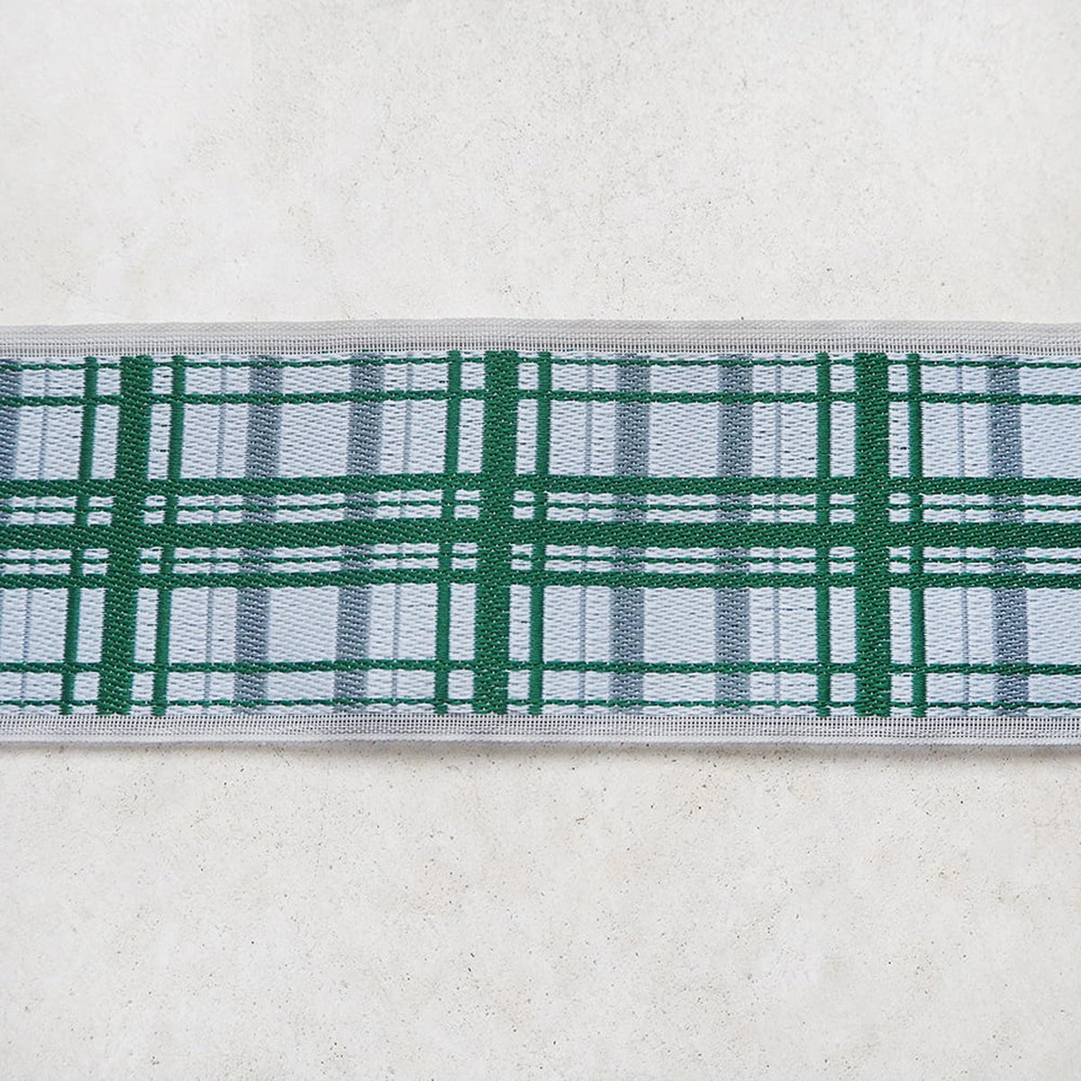 A close-up view of a decorative fabric with a green and white plaid pattern, displayed on a plain white surface.