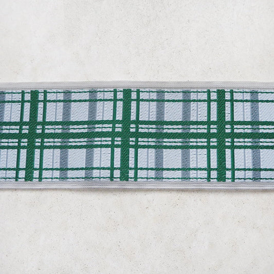 A close-up view of a decorative fabric with a green and white plaid pattern, displayed on a plain white surface.