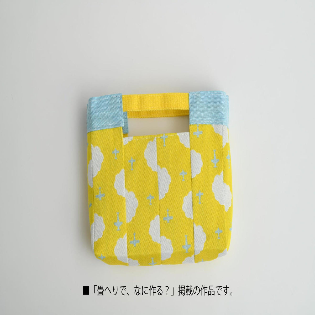 A yellow and blue handbag with a cloud pattern printed on it, placed on a white background.