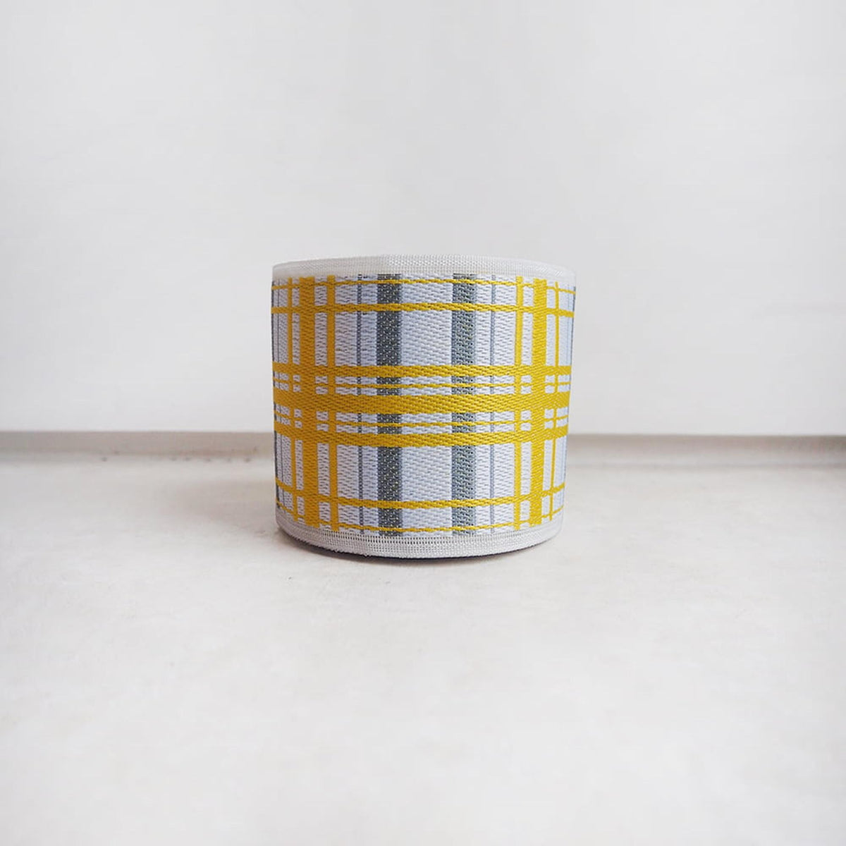 A white mug with a yellow and gray plaid pattern on it, sitting on a white surface.