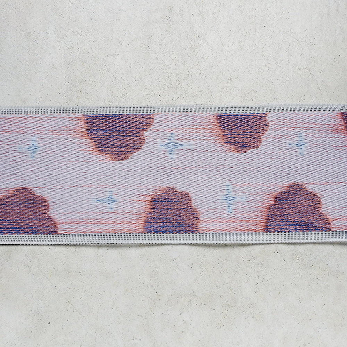 a close-up view of a fabric with a repeating pattern of red and blue shapes, resembling a cloud or a design.