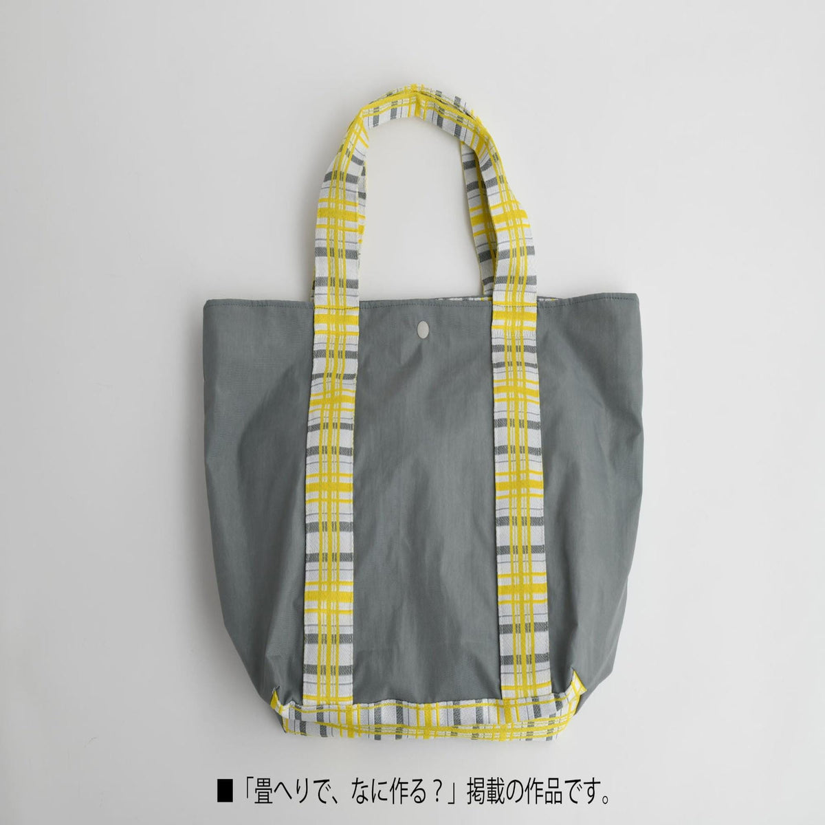 A gray tote bag with a yellow and white plaid pattern on the straps, placed on a white background.