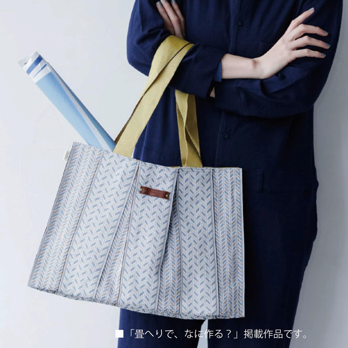 A person wearing a navy blue jacket and holding a patterned tote bag with a yellow strap.