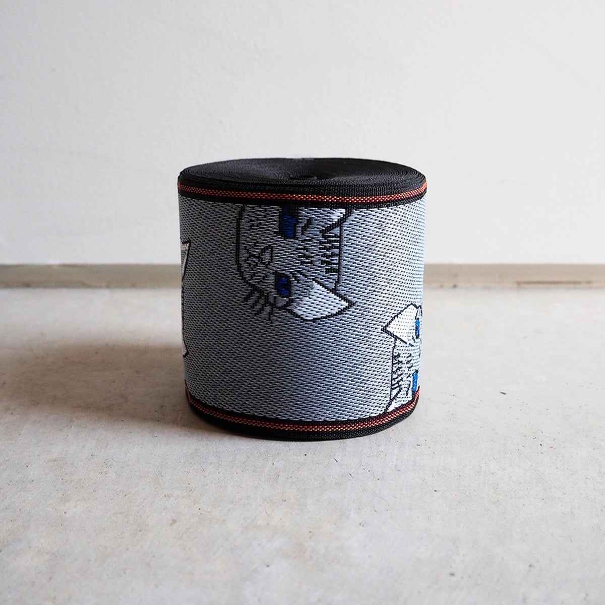 A cylindrical object with a black and gray striped pattern, featuring a cat design on it, placed on a white surface against a plain background.